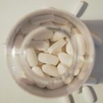 Overhead view of white pills inside a glass jar on a light surface, emphasizing healthcare and medication themes.