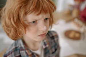 A young boy with curly red hair and flour on his nose, captured in a close-up portrait indoors.