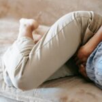 Crop anonymous barefoot female in casual outfit lying on couch while having acute stomach ache