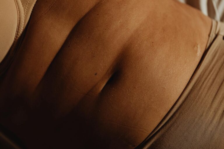 Detailed closeup of a woman's abdomen and bellybutton in beige underwear, showcasing skin texture.