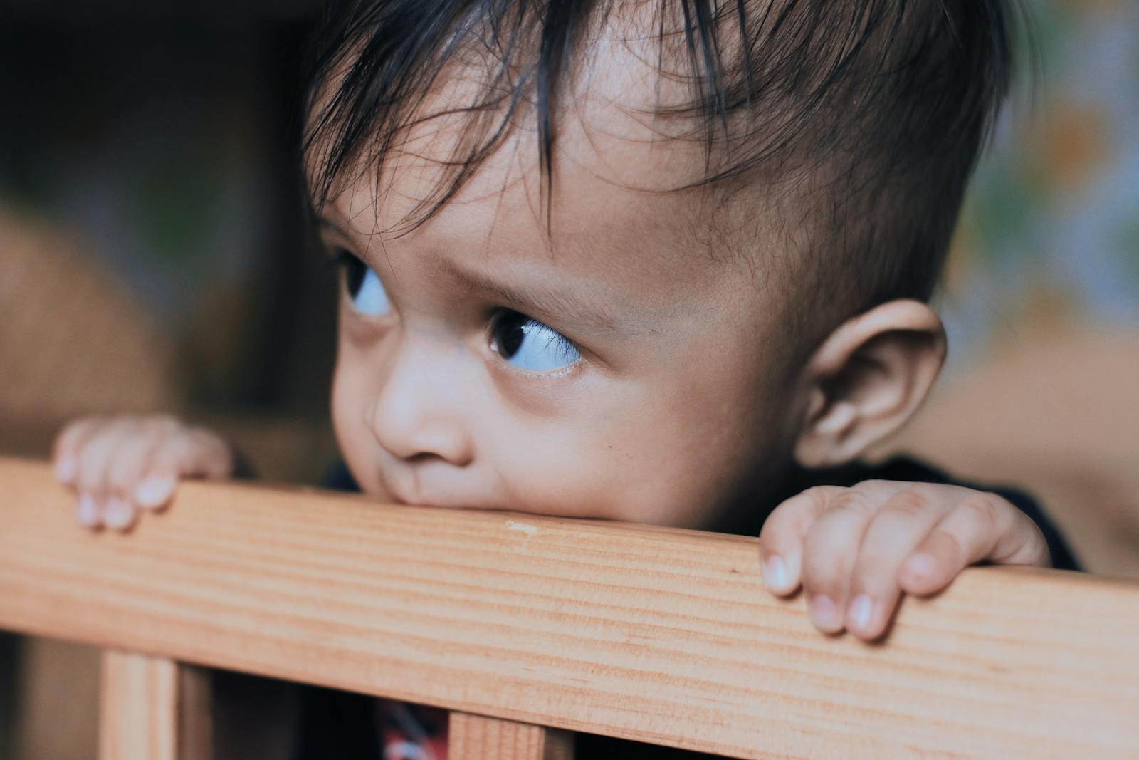 Adorable toddler biting a wooden crib rail, showcasing innocence and curiosity indoors.