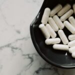 Close-up of white capsules in a black bowl on a marble surface, symbolizing healthcare and medication.
