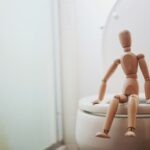 brown wooden doll on white ceramic toilet bowl