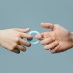 Close-up of two hands exchanging a blue silicone ring against a soft background.