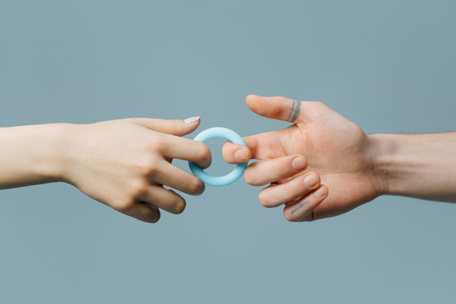 Close-up of two hands exchanging a blue silicone ring against a soft background.