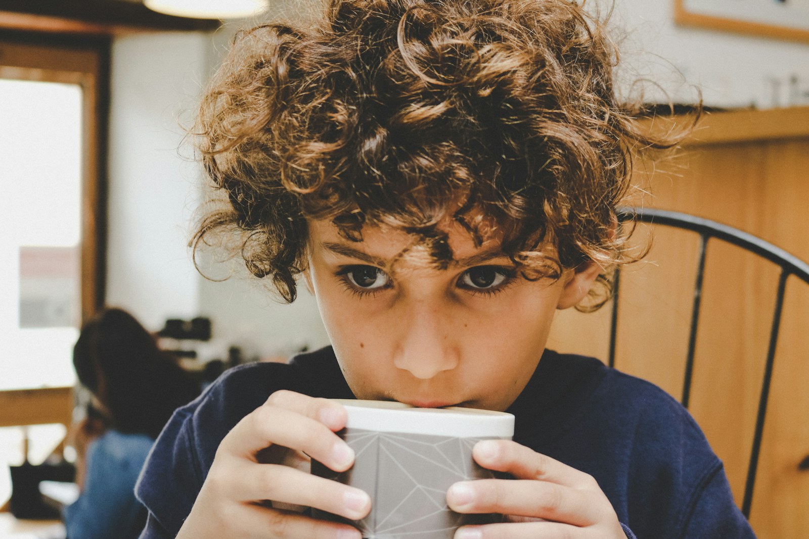 boy in blue long sleeve shirt holding white ceramic mug