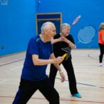 Seniors playing badminton in a gymnasium