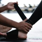 Jak ćwiczyć staw skokowy po kontuzji? Close-up of an athlete's ankle being wrapped with an elastic bandage in a gym setting.